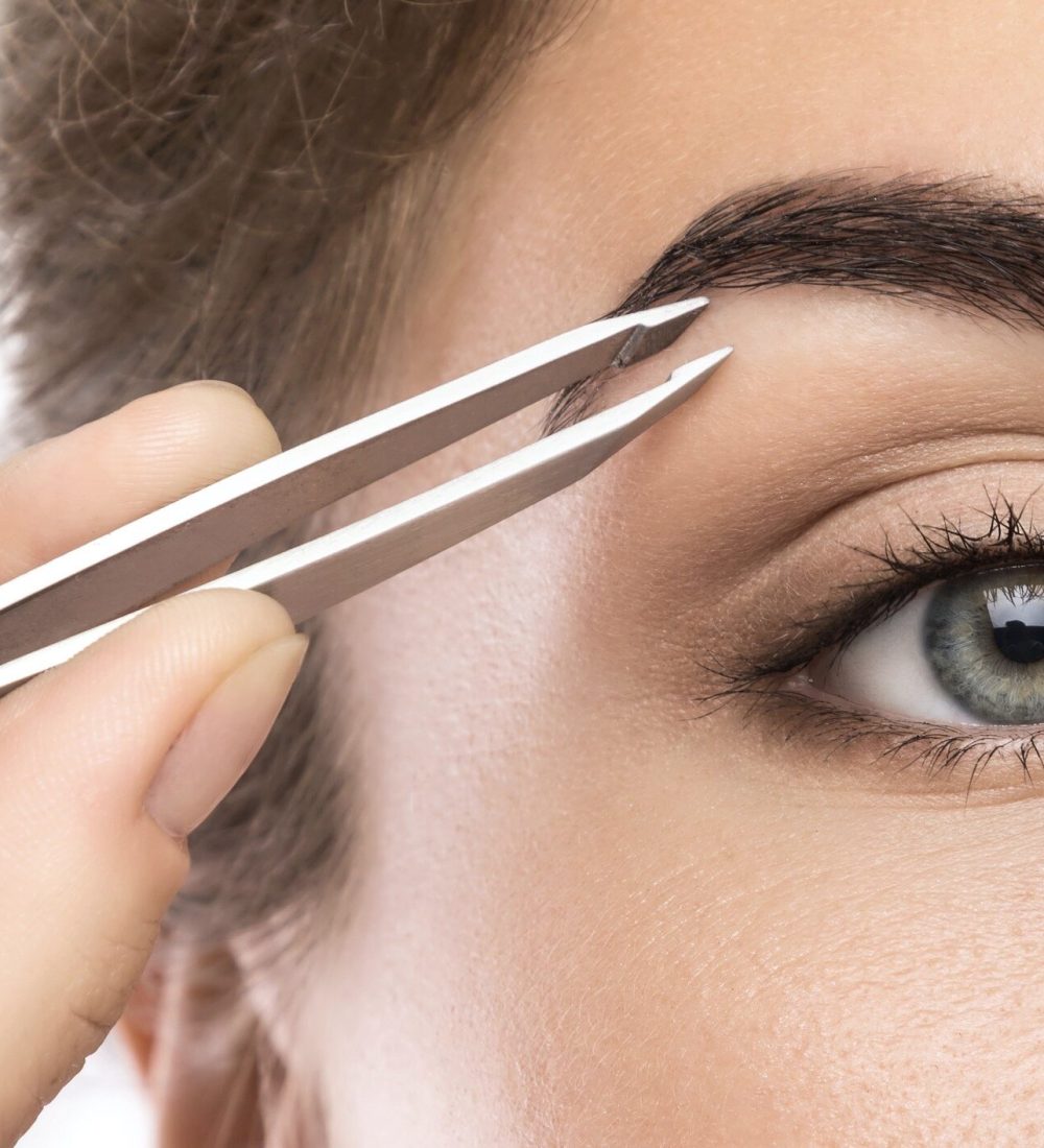 Close up of female face and eyebrow with tweezers